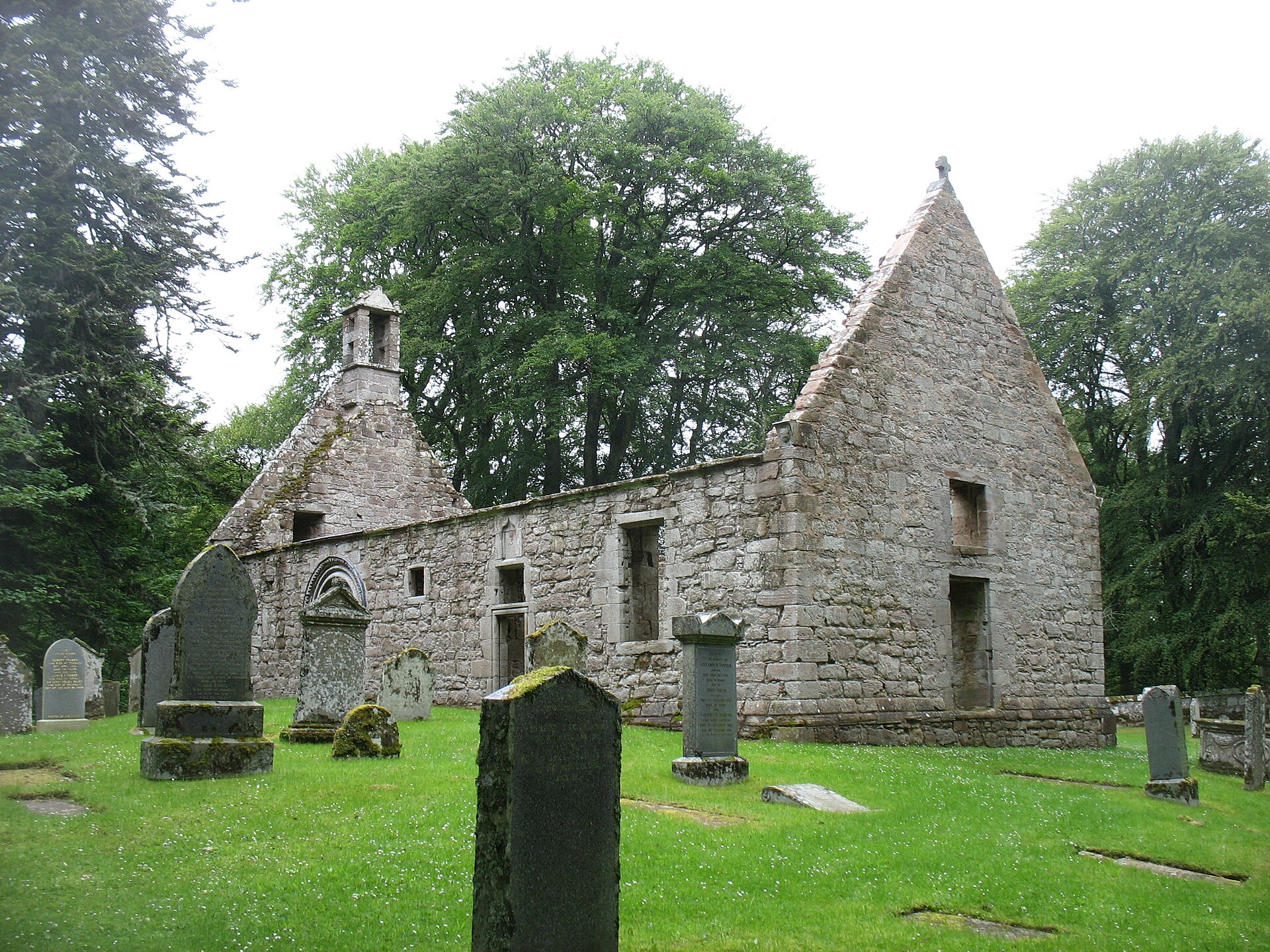 The roofless kirk of St Mary at Auchindoir among its gravestones and trees.