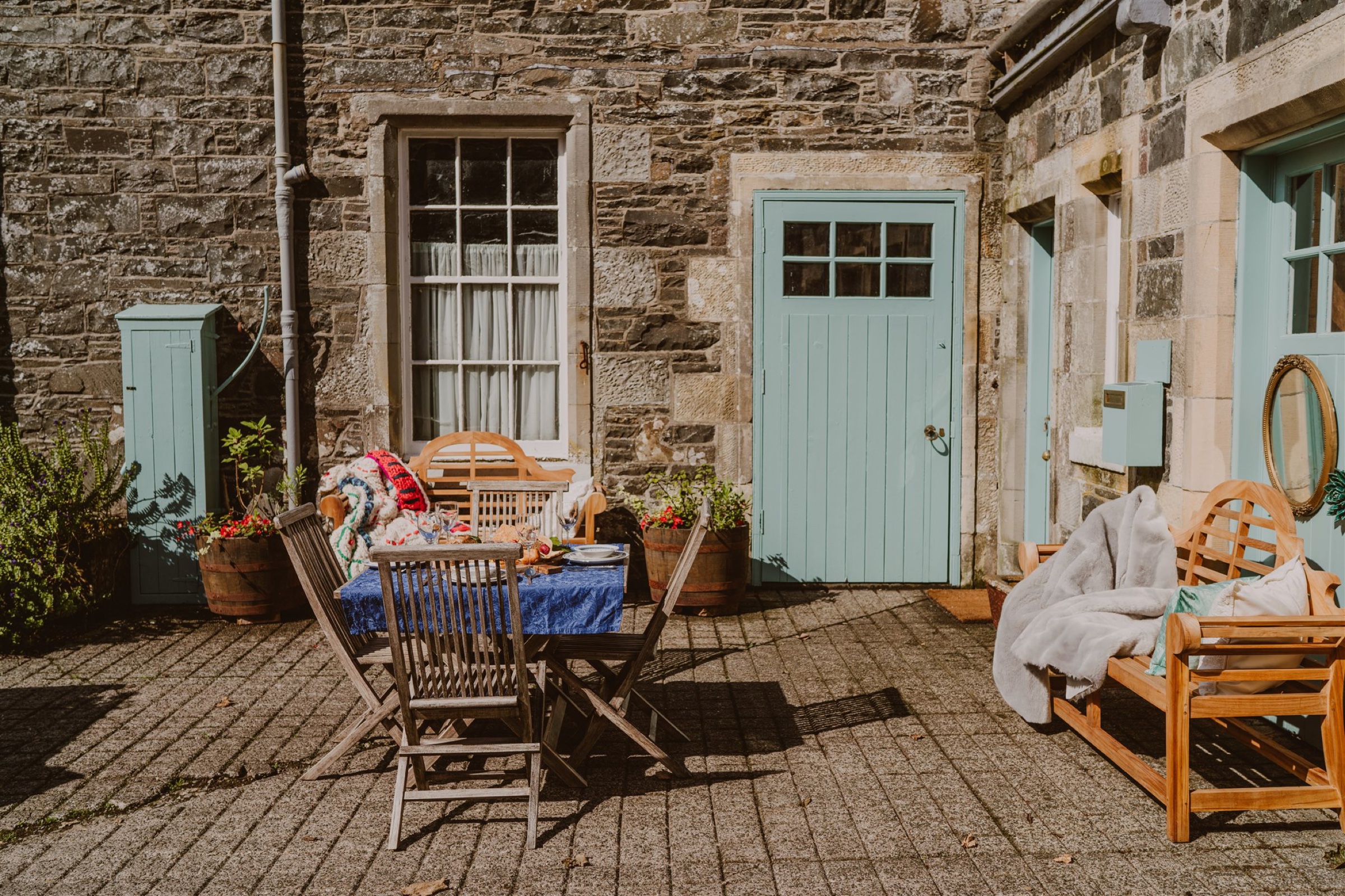 Heritage Coachman Lodge's pale blue door in the cobbled stable courtyard, a table and a wooden bench in the sun outside.