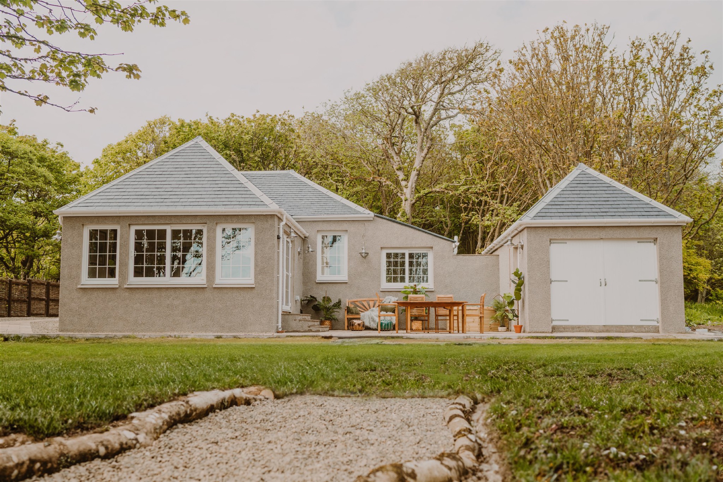 Saltwater Chronicles Lodge, a grey lodge with an outbuilding beside it, seen across the lawn from a gravel path.