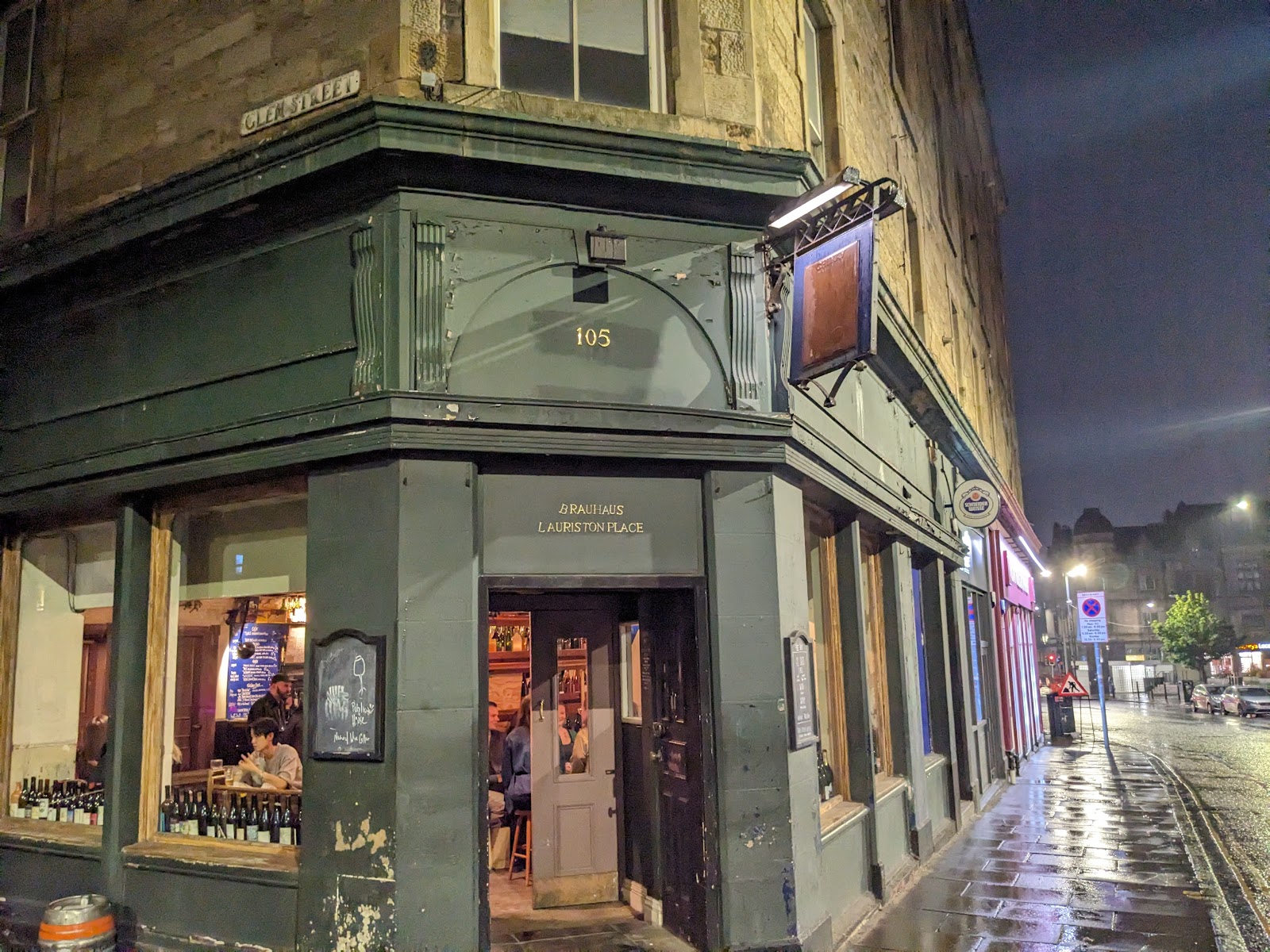 The dark green corner front of Lauri at 105 Lauriston Place on a wet evening, with wine bottles in the lit windows and drinkers inside.