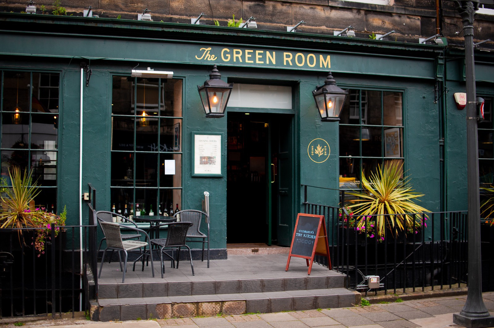 The dark green front of the Green Room on William Street, with lanterns, plants and tables on the steps.
