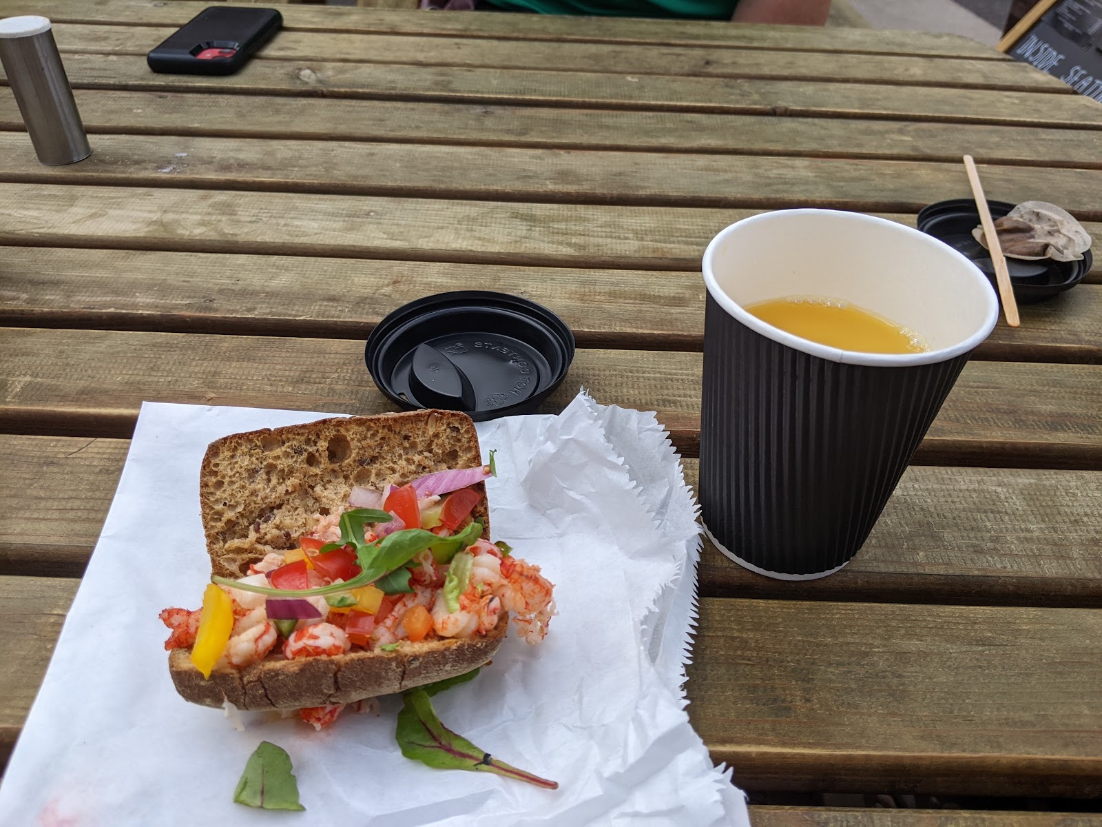 Prawn and salad roll beside a takeaway cup of juice on a picnic table