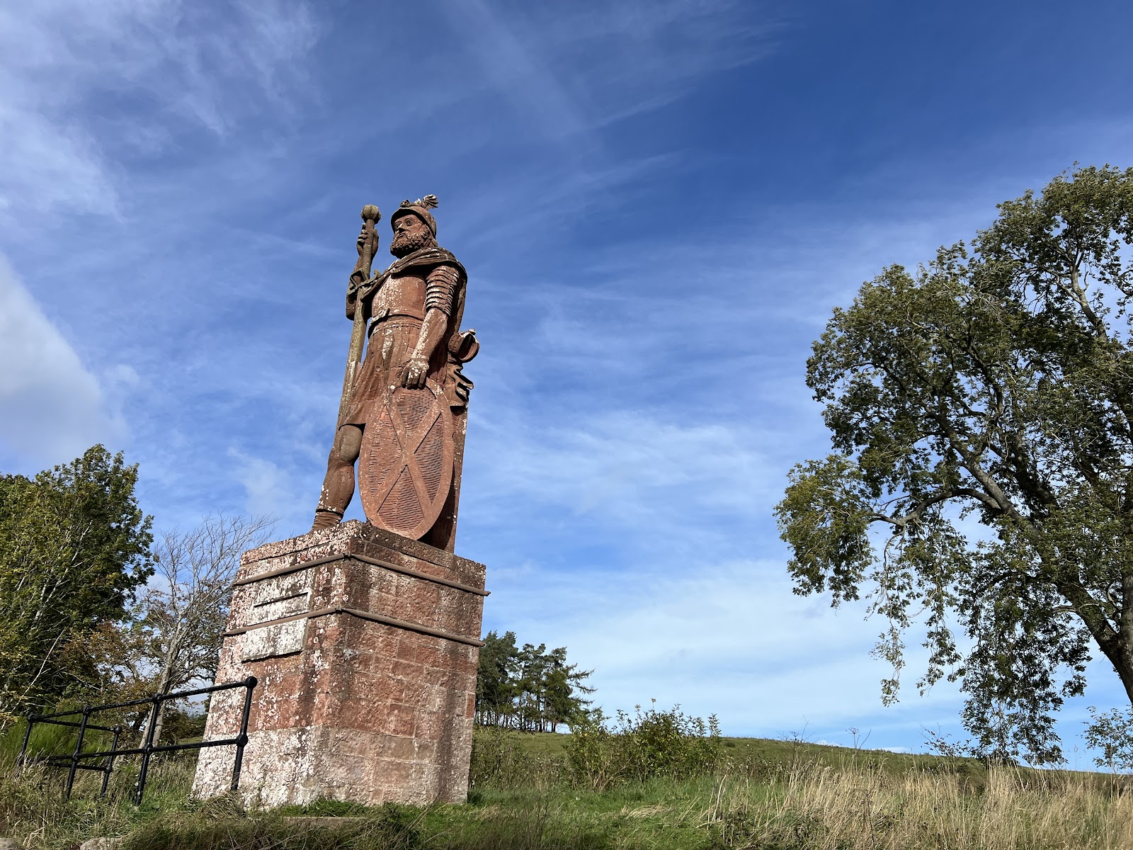 The giant red sandstone statue of William Wallace with sword and shield on a tall plinth against a blue sky.