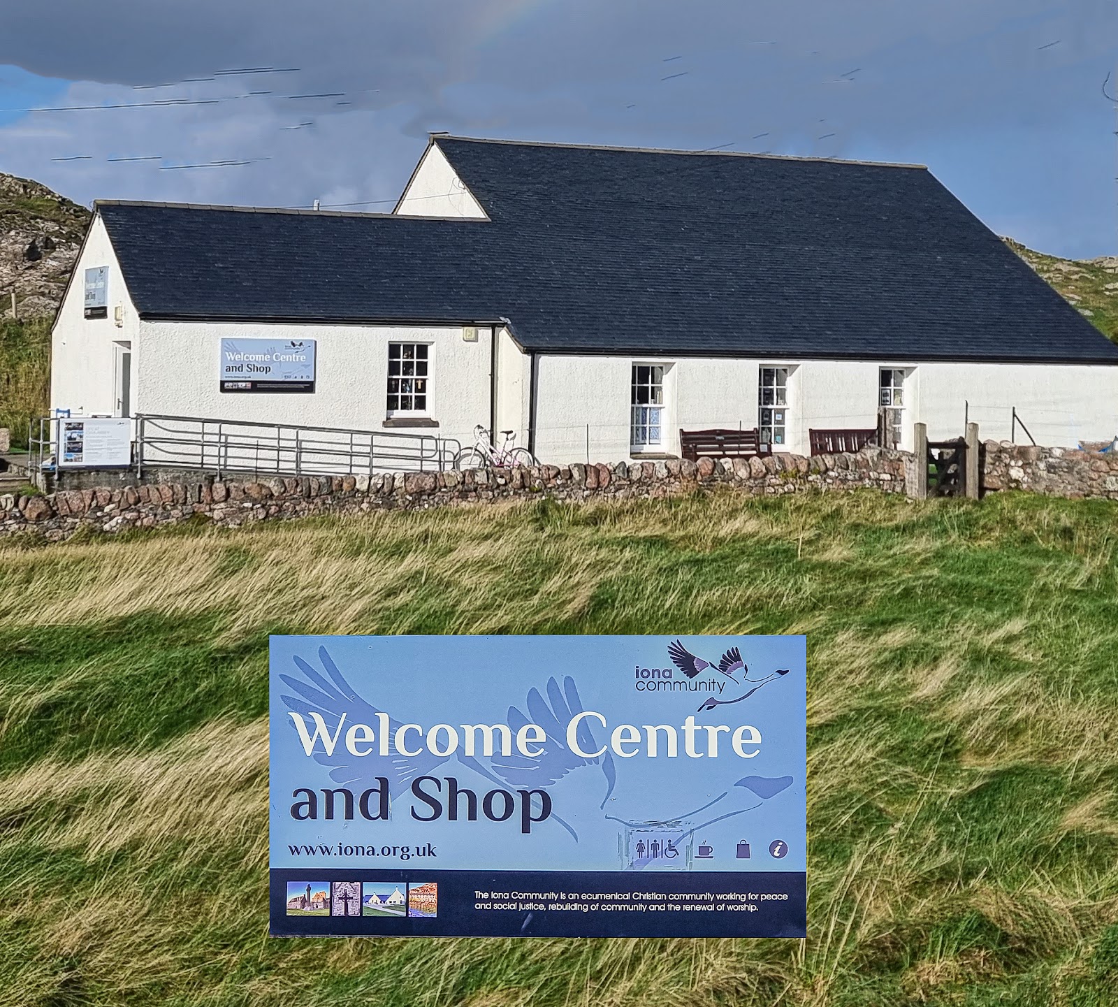 The Iona Community's Welcome Centre and Shop, a low white building with its sign on the grass in front.