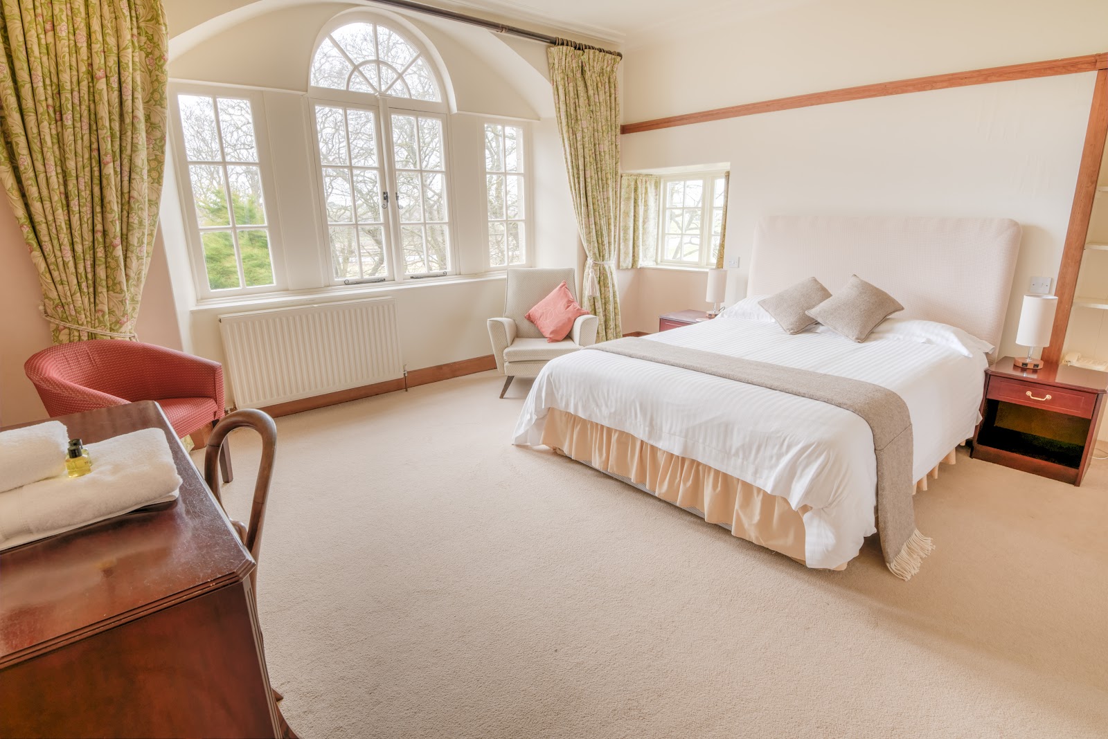 Bedroom with arched window, double bed and armchairs beside a wooden dresser