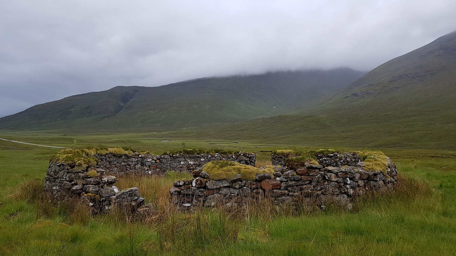 A low stone enclosure on the grassy floor of Glen Shiel, the steep hillsides rising into cloud behind.