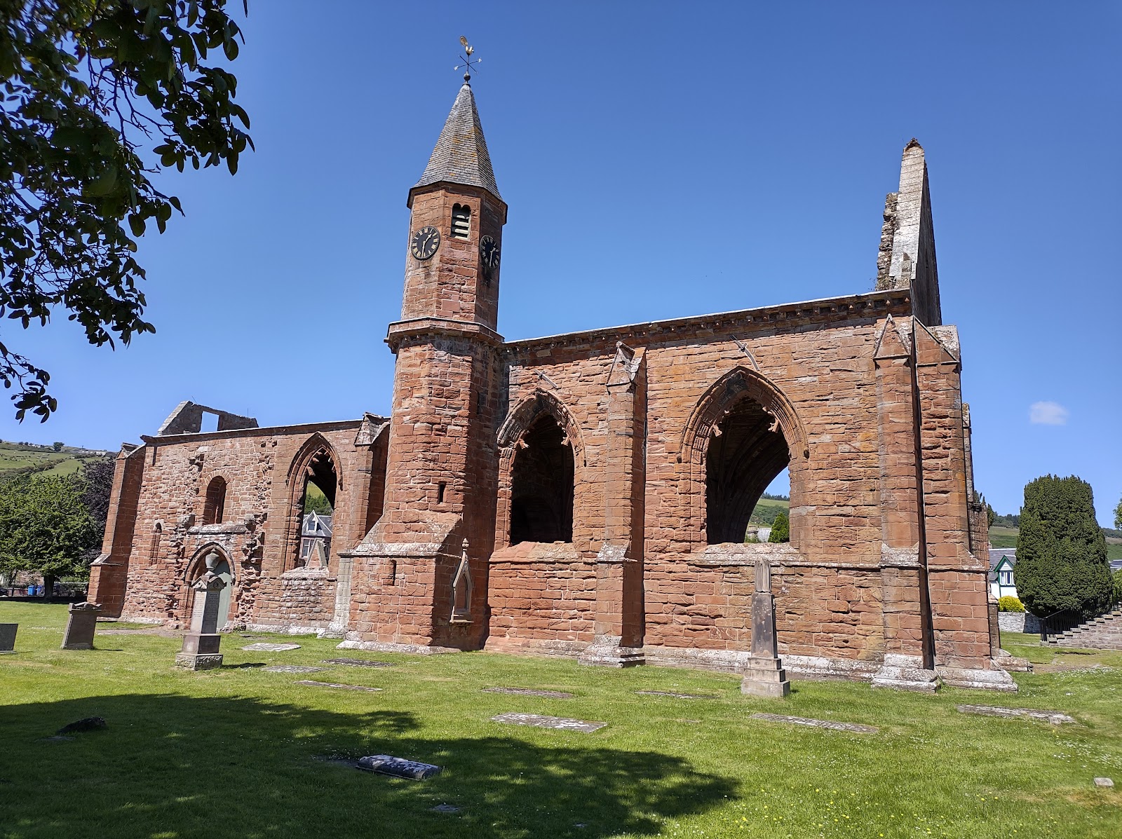 Fortrose Cathedral's red sandstone arches and clock tower in its green square under a blue sky.