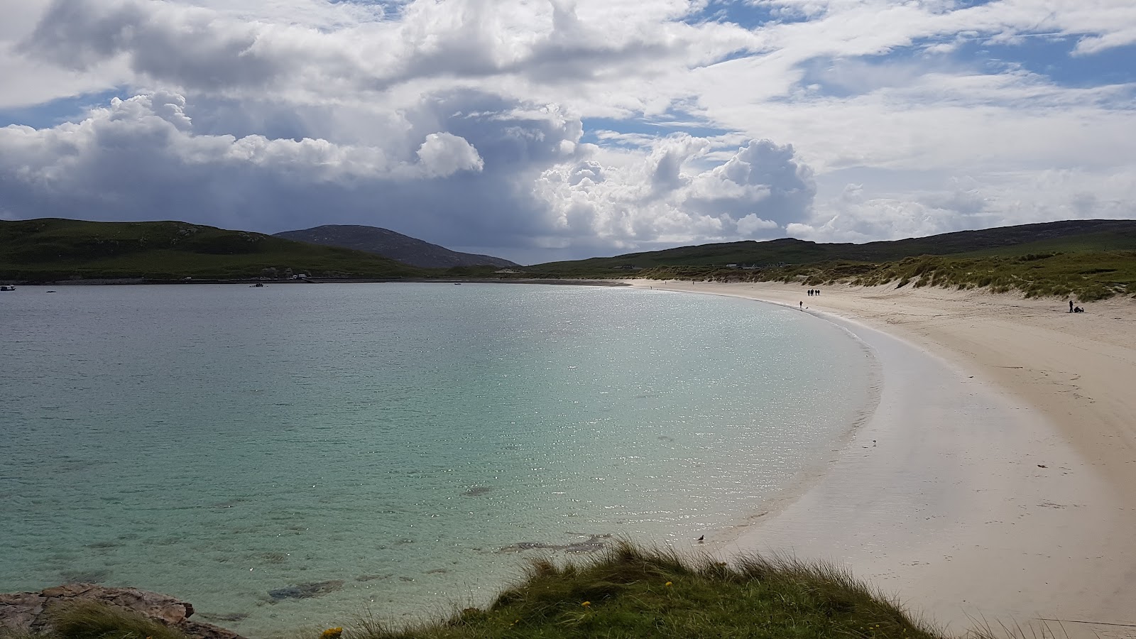 Turquoise bay curves into a white sandy beach with distant walkers and hills