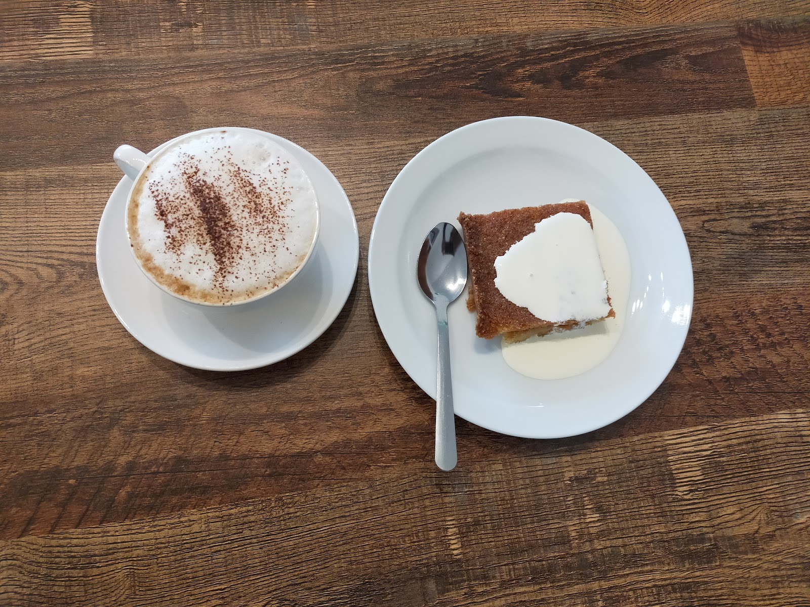 A cappuccino and a slice of iced cake on white plates at Polly Kettle.
