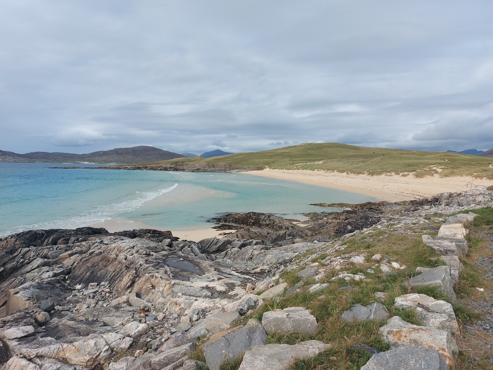 Nisabost beach from the rocks, white sand and turquoise water below green dunes.