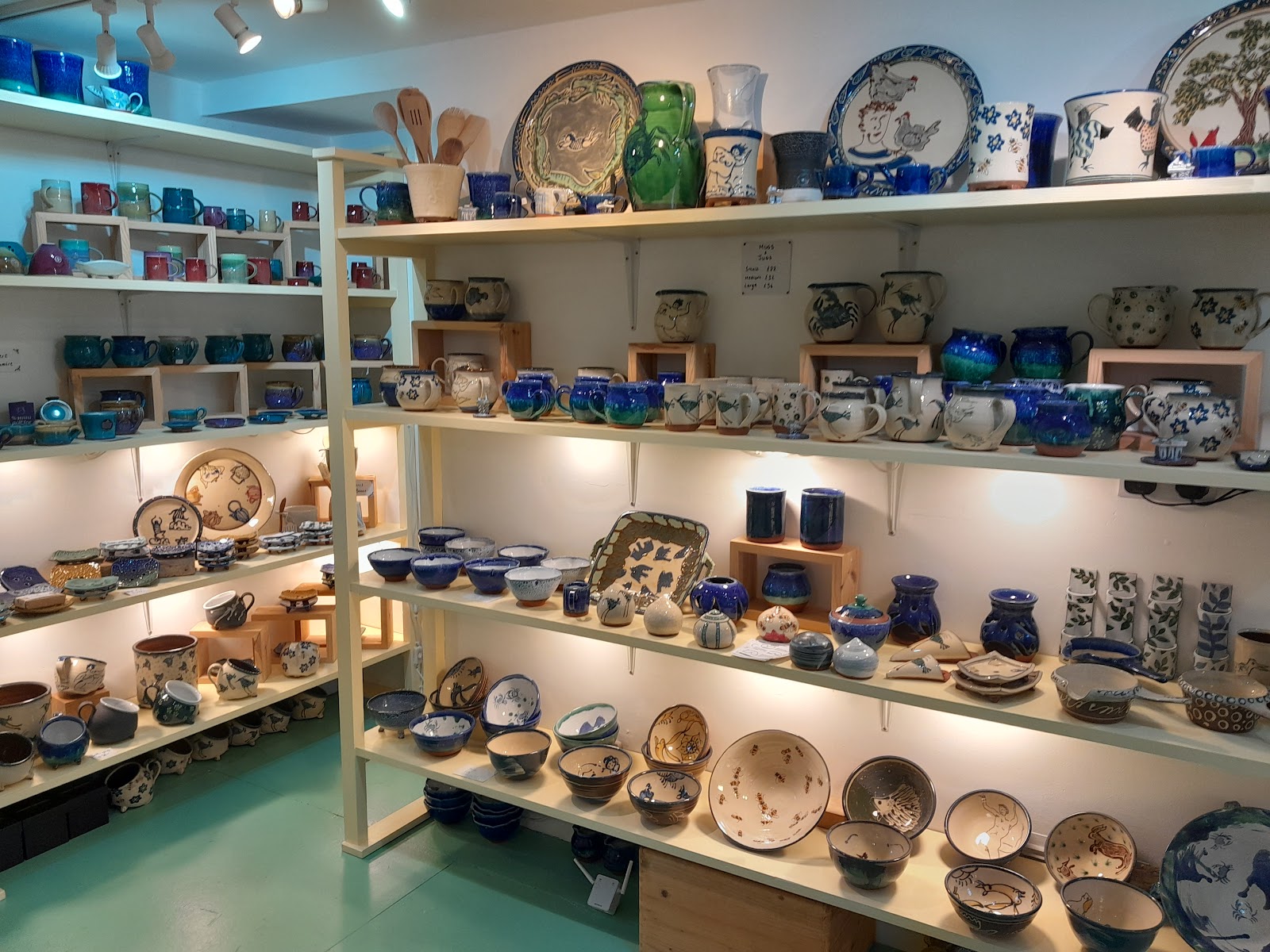 Lit wooden shelves of handmade pottery, bowls and plates inside gallery48 in Cromarty.