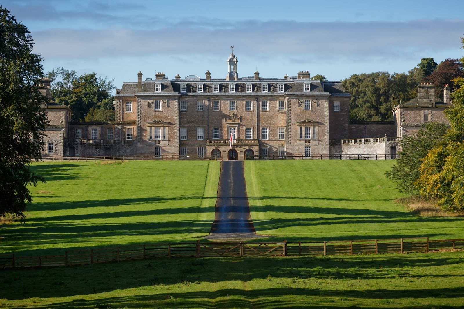 Marchmont House at the end of its long lawn, a pale Palladian front with a central cupola under a blue sky.
