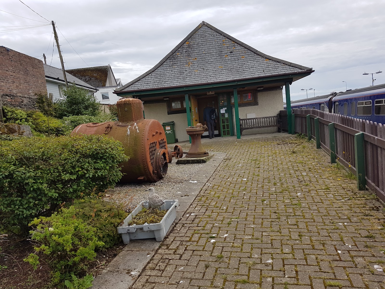 The Mallaig Heritage Centre, a low building under a pitched slate roof beside the railway platform, a brick path and planters in front.