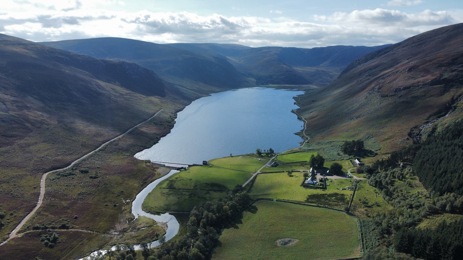 Aerial view of a loch feeding a river through a glen with green fields