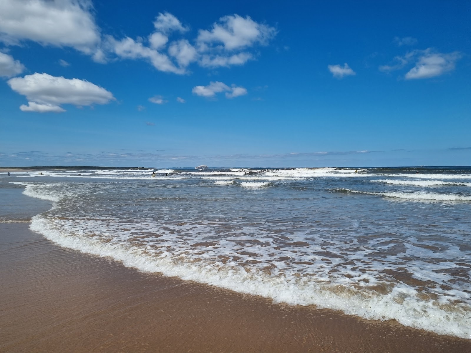 Waves breaking on a sandy beach under a blue sky with scattered clouds