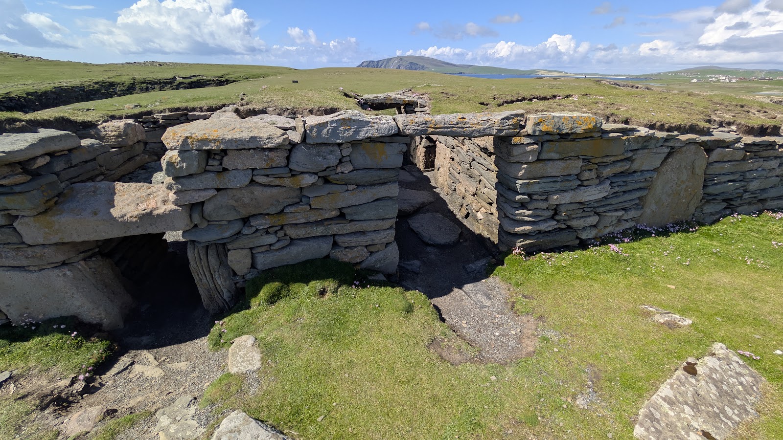 The stone walls and low passage of the Ness of Burgi blockhouse on its grassy headland.