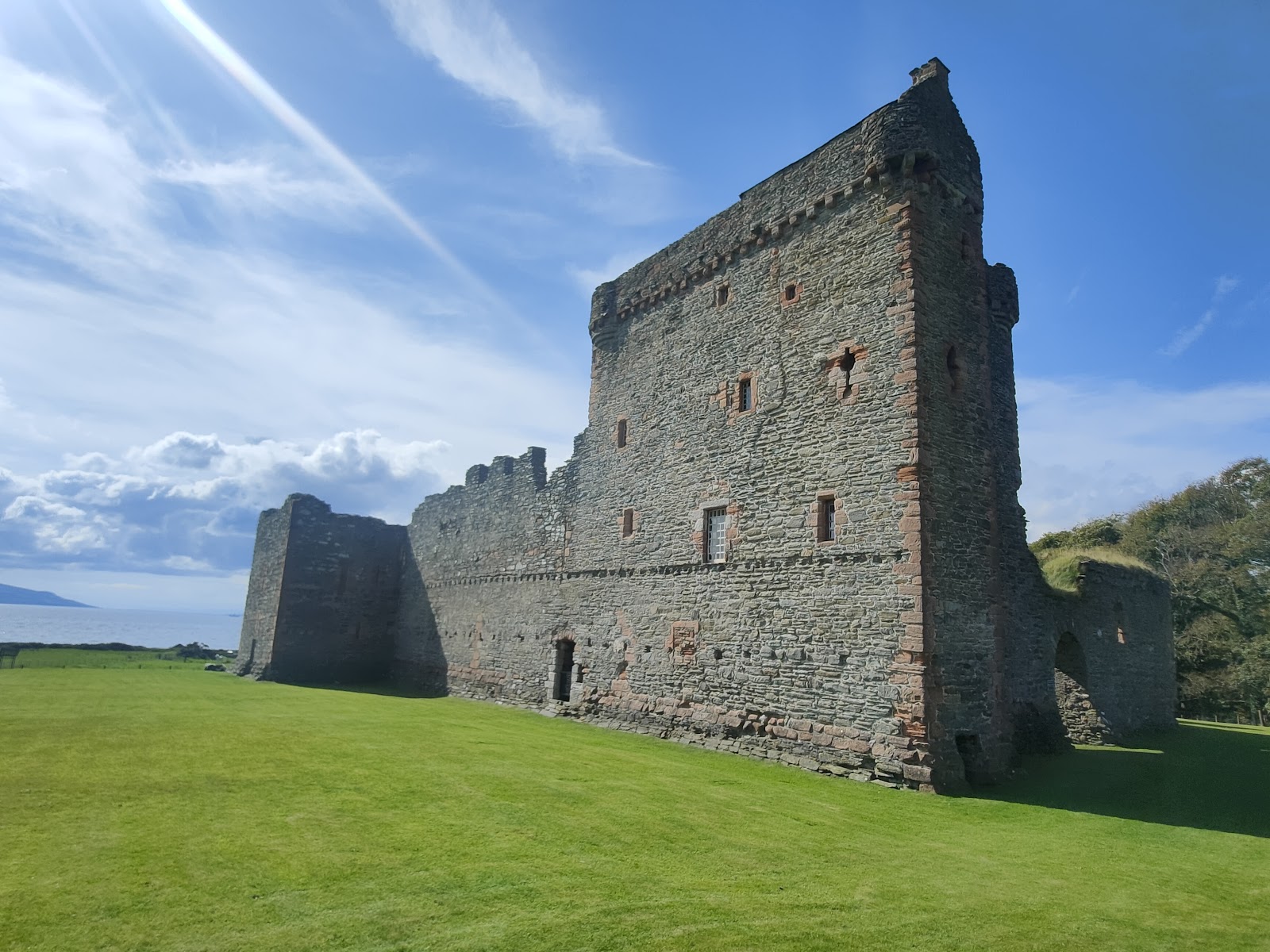 Ruined stone tower house stands on grass beside the coastline