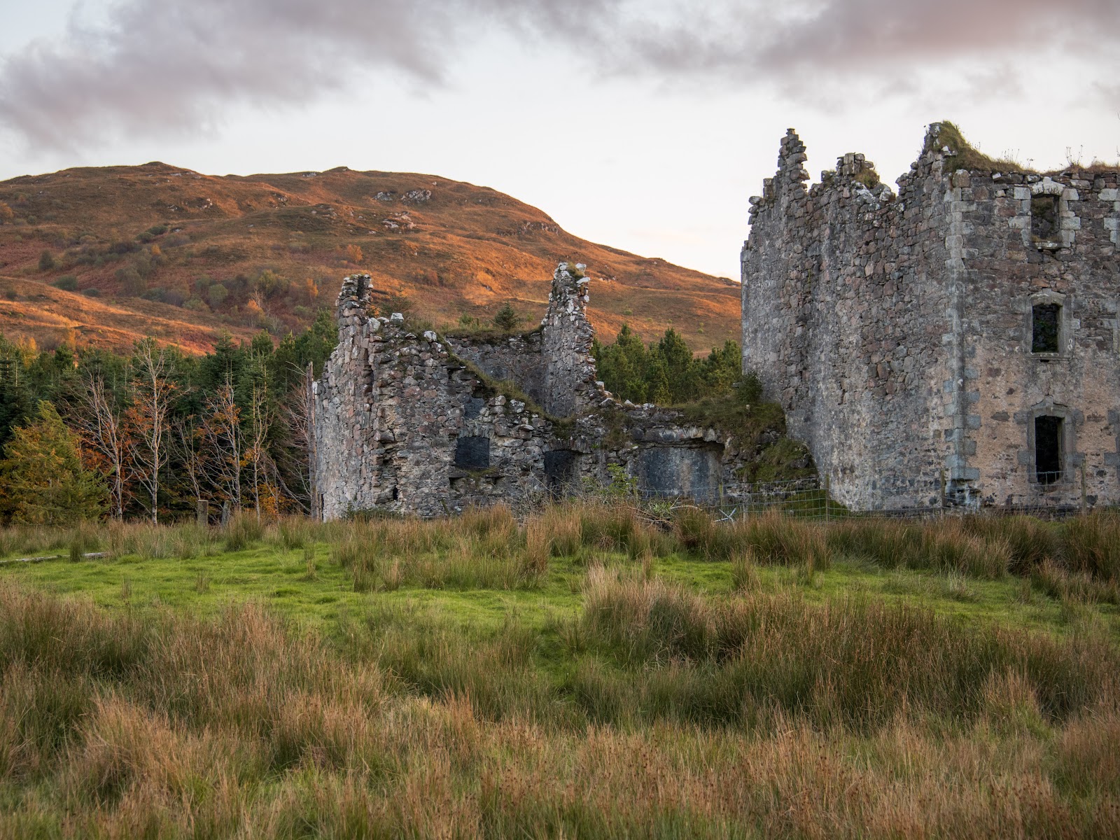 The roofless stone ranges of Bernera Barracks standing in rough grass with a hill behind.