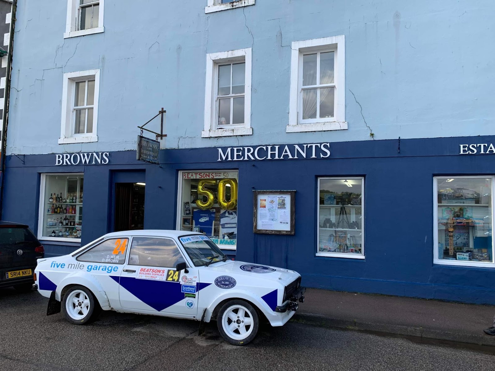 The blue front of Brown's on Tobermory's Main Street, a rally car parked outside.