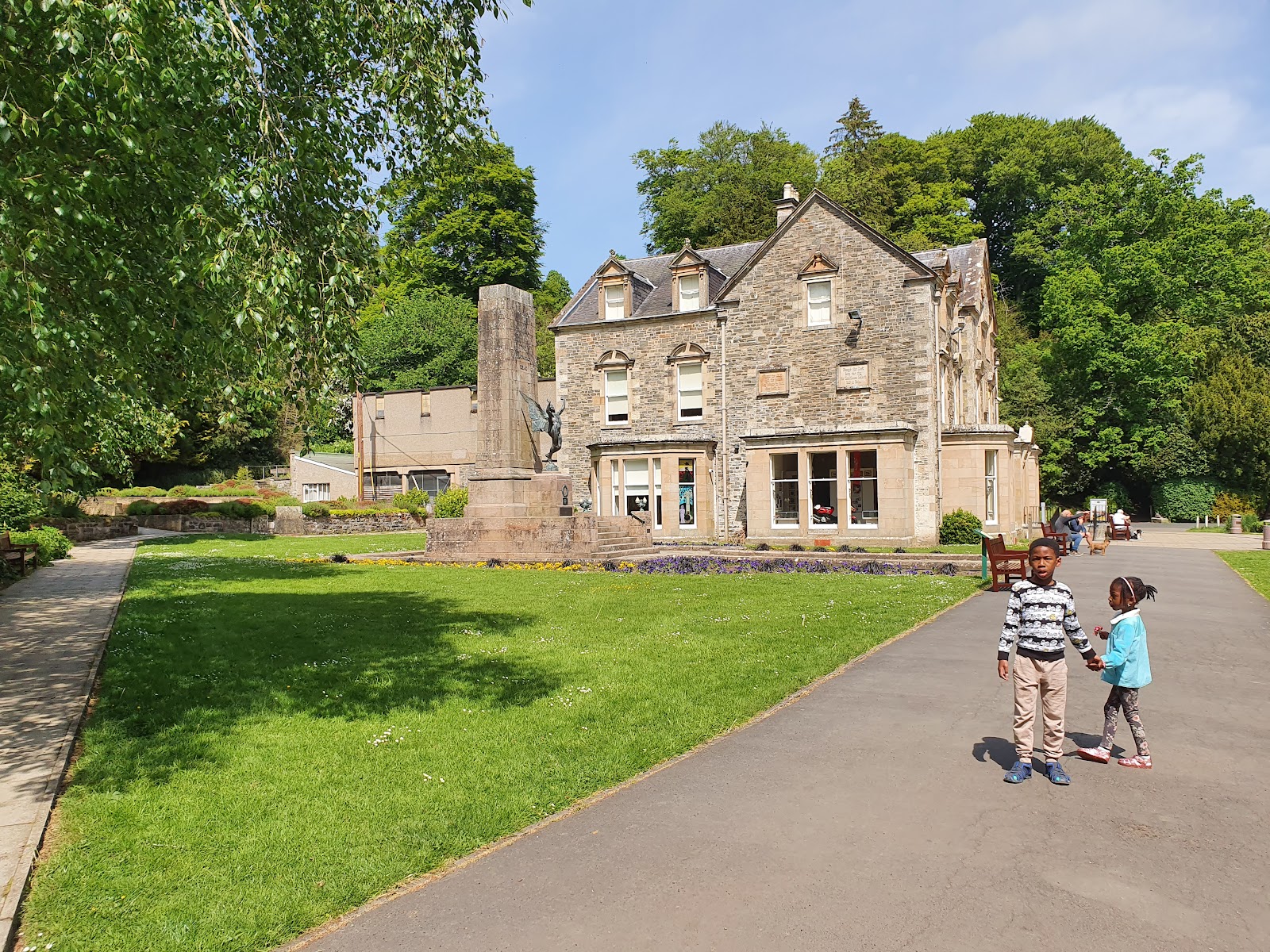 Children walk past a war memorial in front of a stone mansion