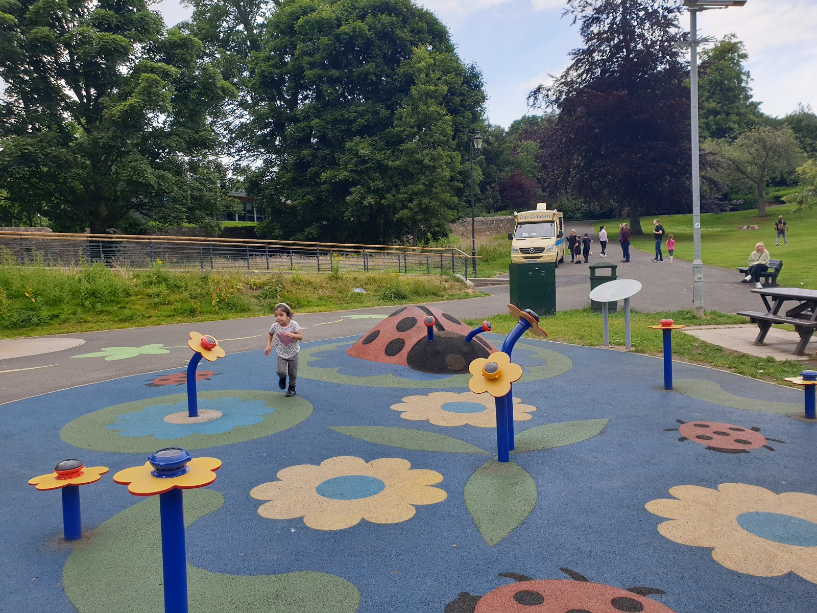 Child runs across a ladybird-themed play park, ice cream van parked behind