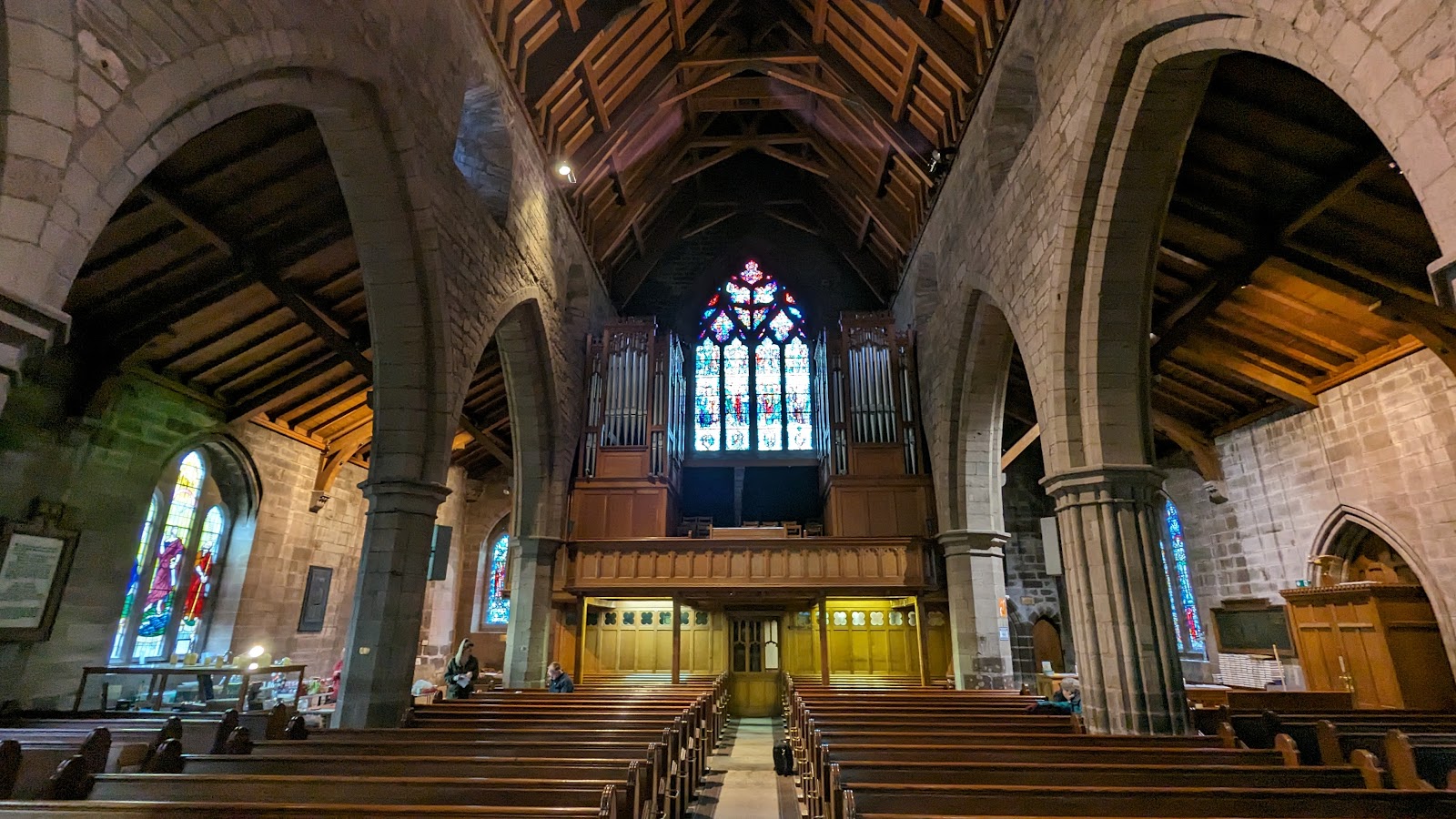 Church nave with wooden pews facing a stained glass window and organ pipes