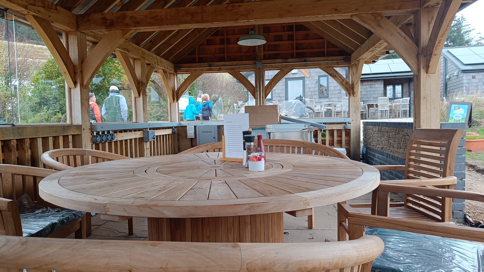 Round teak table under an oak-framed pavilion with a burger menu chalkboard