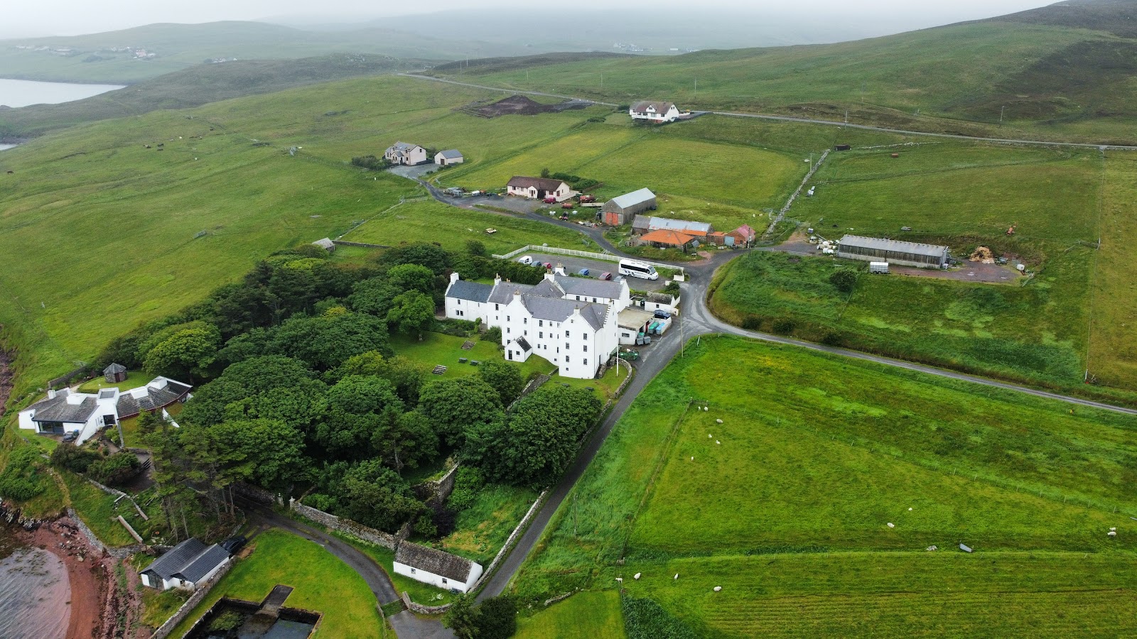 Busta House among trees on the shore, with fields and the voe beyond.