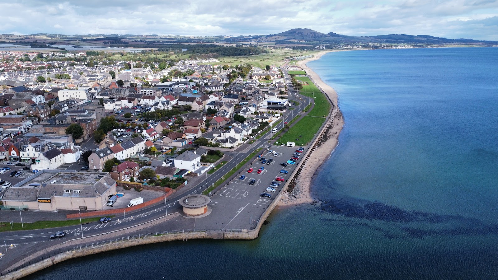 Aerial view of a coastal town's promenade and sandy shoreline curving towards distant hills