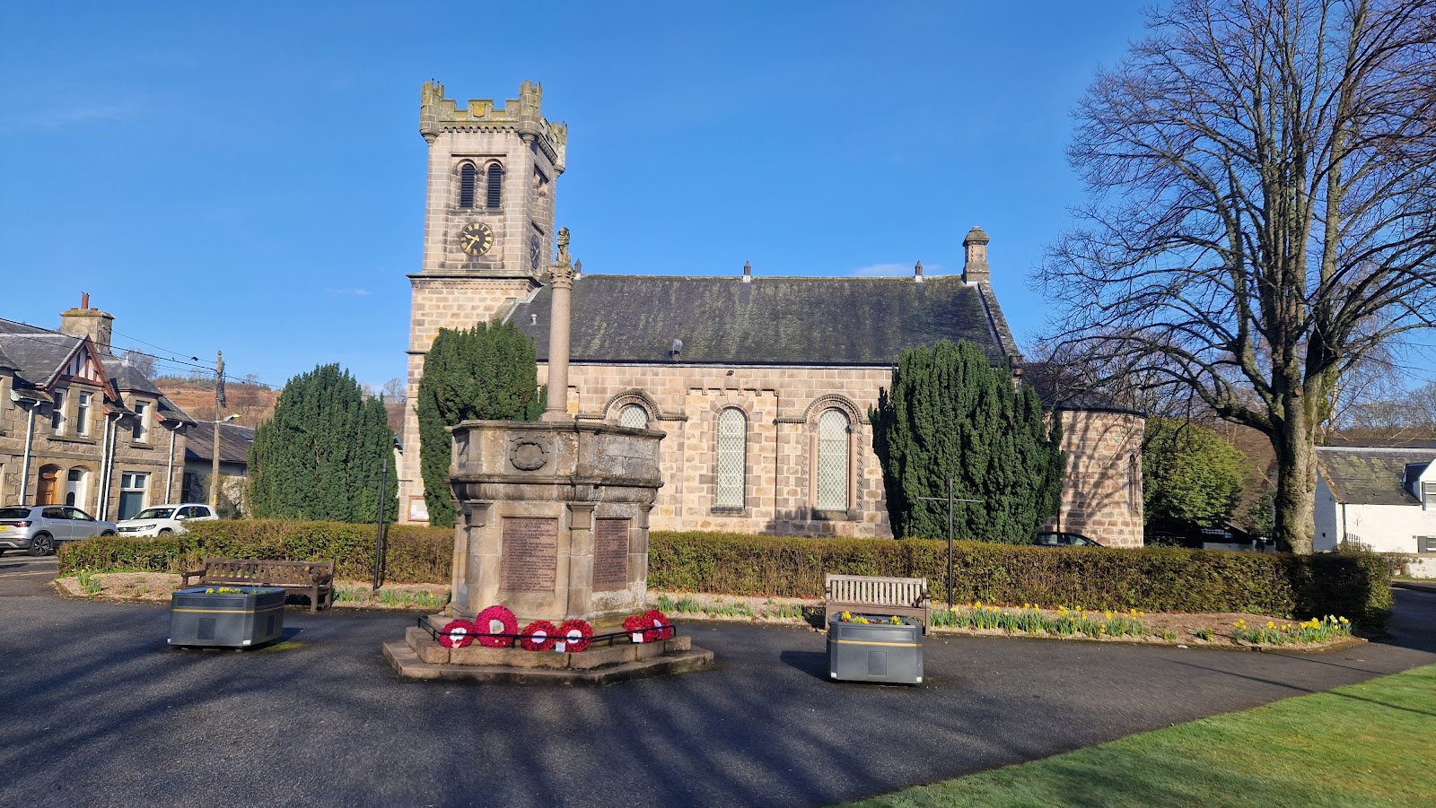 War memorial with poppy wreaths in front of a stone church tower