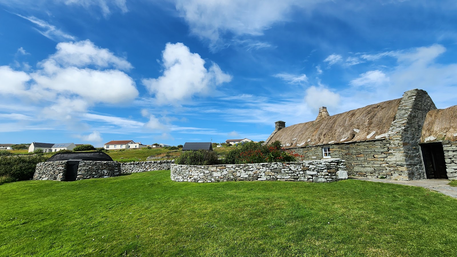 The long thatched Crofthouse Museum and its stone dykes under a blue sky.