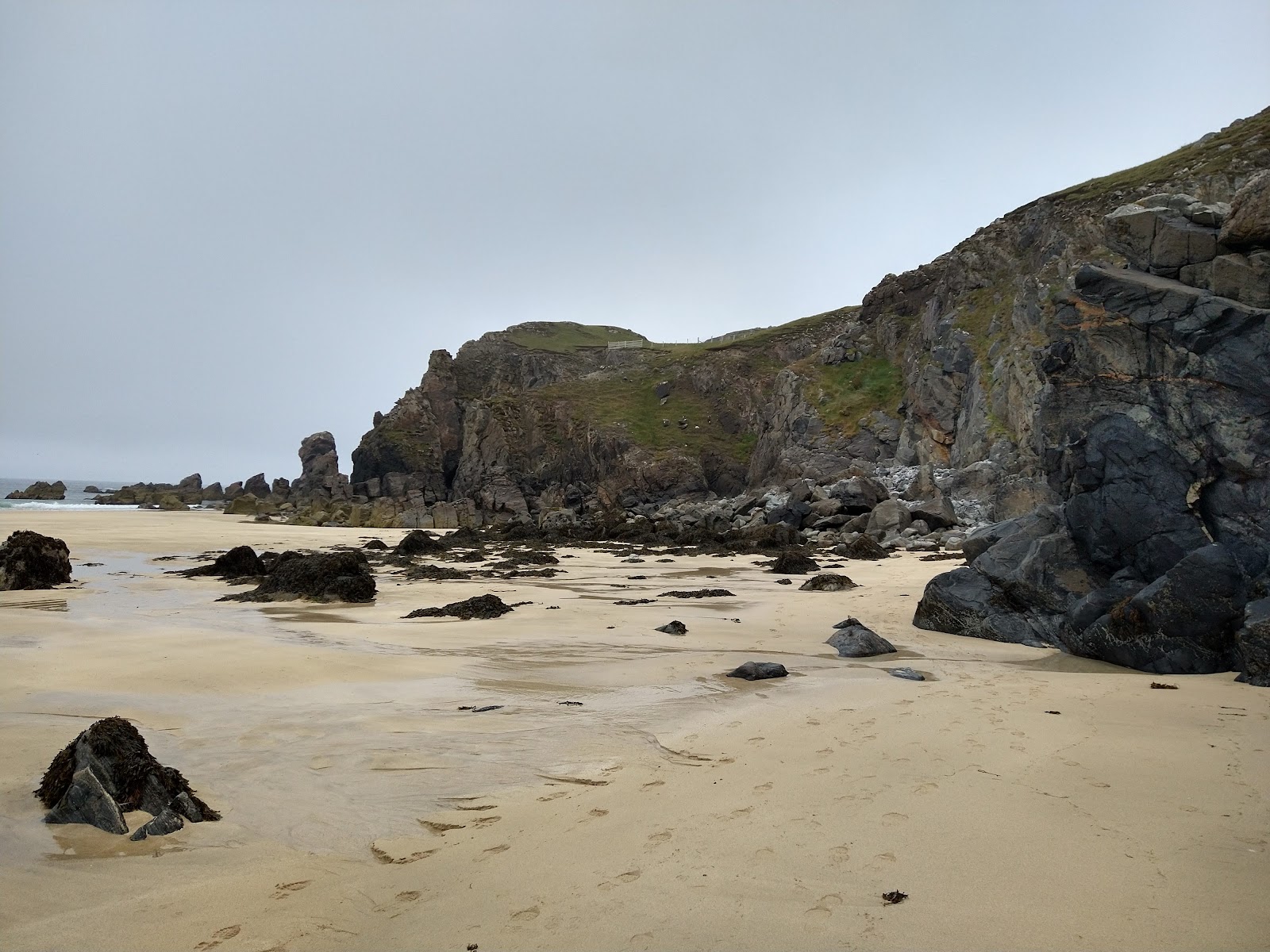 Golden sand and dark rocks at Dalmore Beach below rugged cliffs.