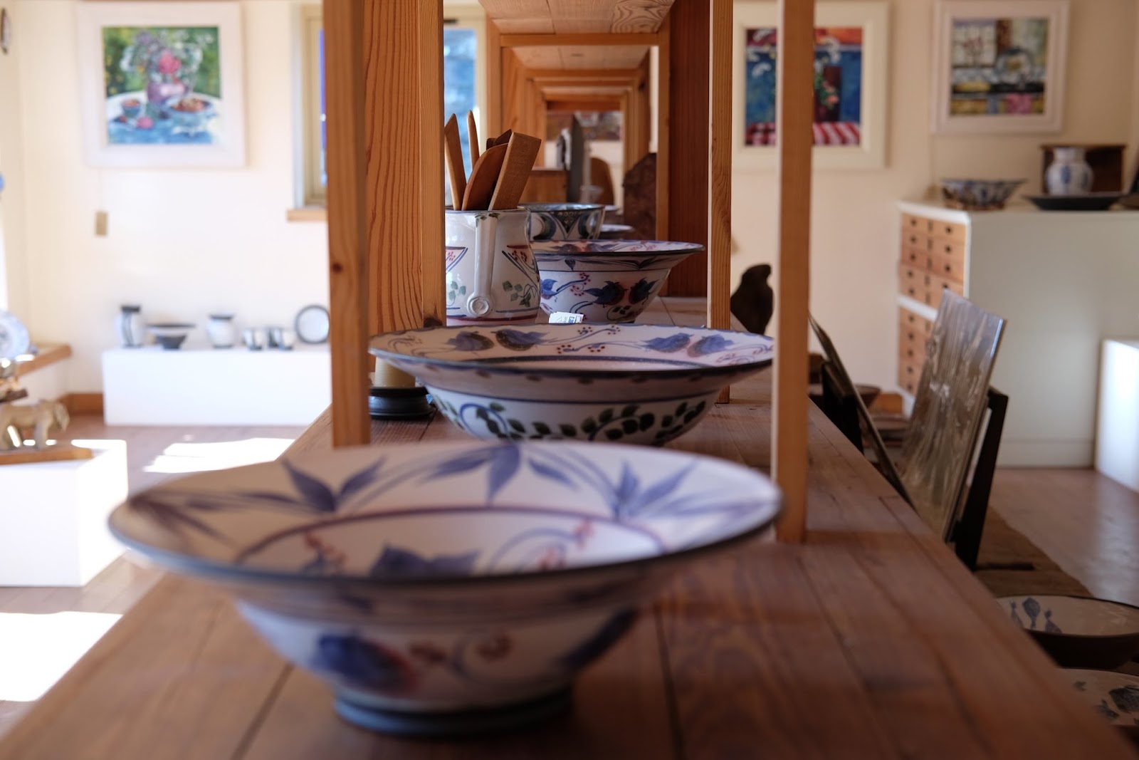 Hand-painted ceramic bowls line a wooden table in a gallery