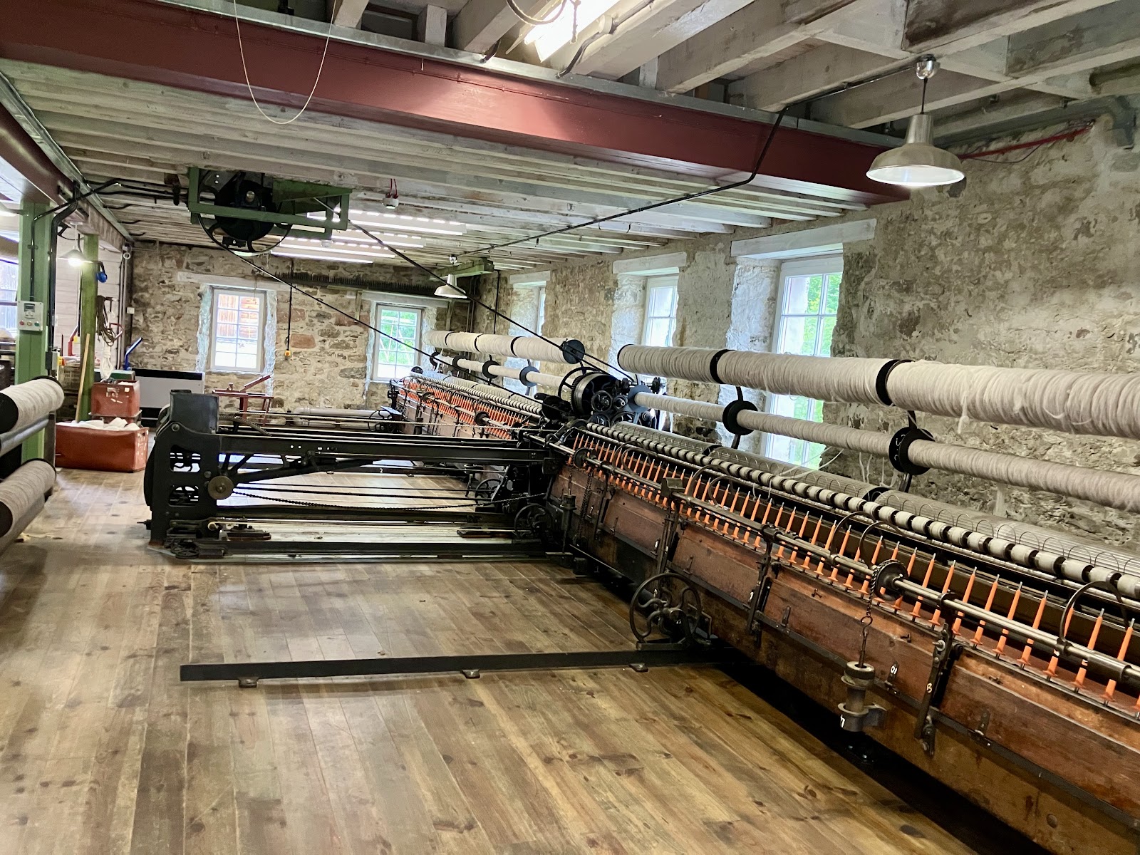 Long spinning frame with wound bobbins fills a stone-walled mill room