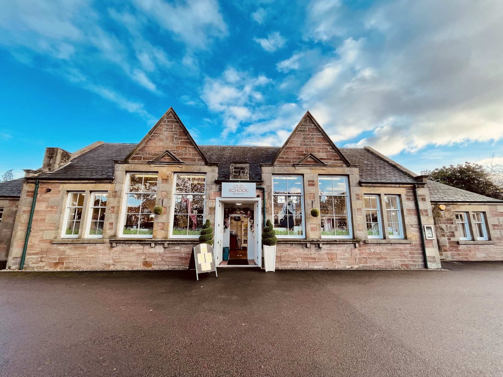 The Old School Beauly, a twin-gabled Victorian stone school on the High Street, under a bright blue sky.