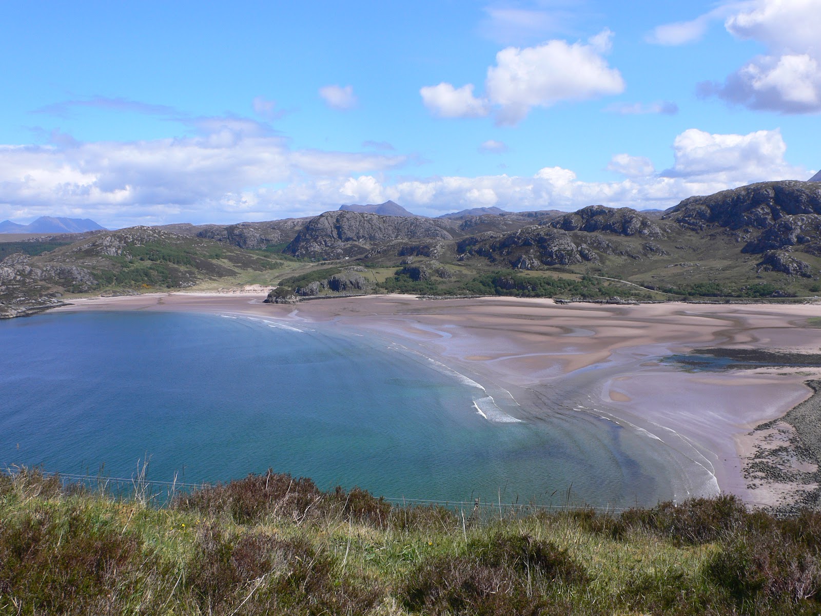 Sandy bay curves between rocky hills, tide out and turquoise water below