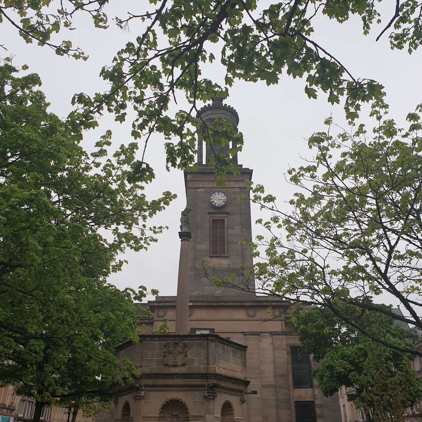 Sandstone clock tower and mercat cross framed by tree branches