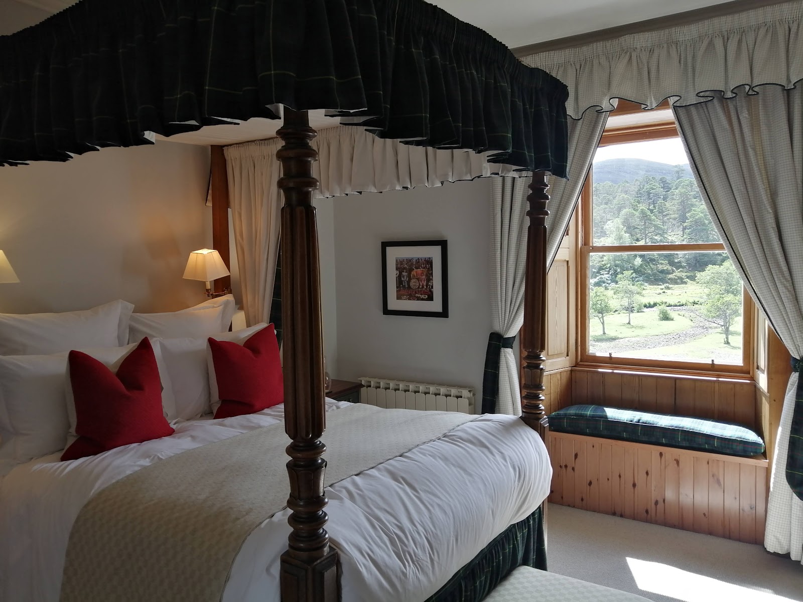 Four-poster bed with tartan canopy beside a window seat overlooking wooded hills