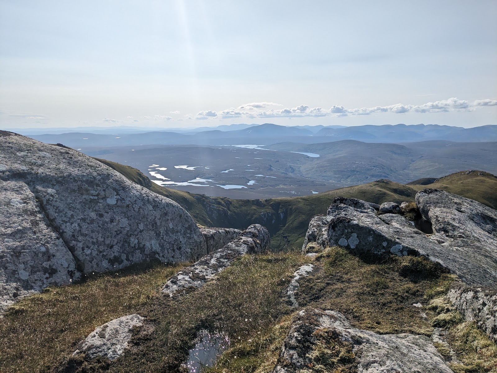 Lichen-covered boulders frame a scattering of lochans across distant Highland glens