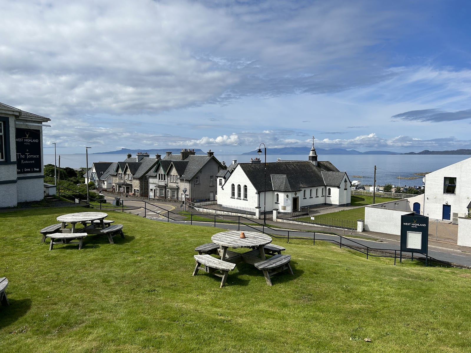 Picnic tables outside the West Highland Hotel overlooking Mallaig's church and coastline