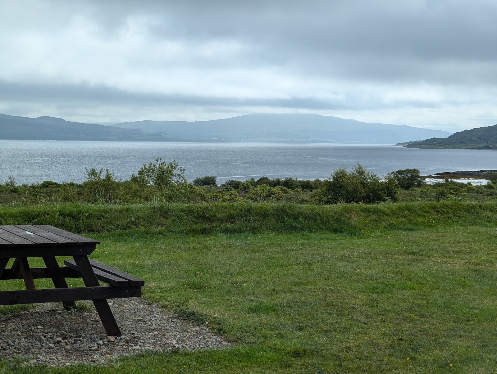 A picnic bench on the grass above Salen Bay, the calm water and hills beyond.