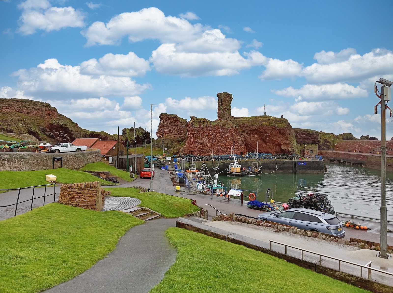 Fishing boats moor beneath Dunbar Castle's red sandstone ruins on the harbour