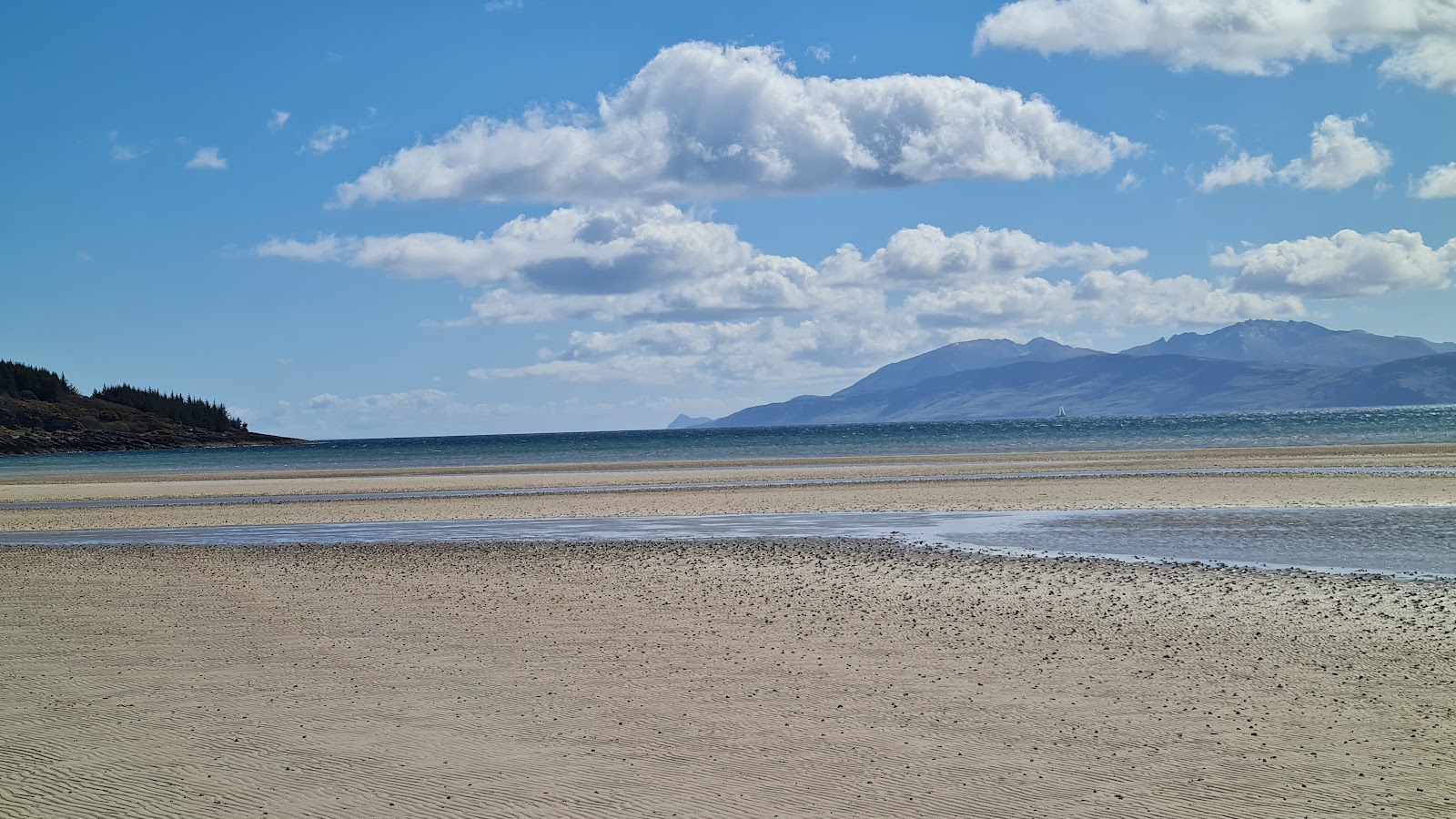 Sandy shoreline at low tide with mountains rising across the water