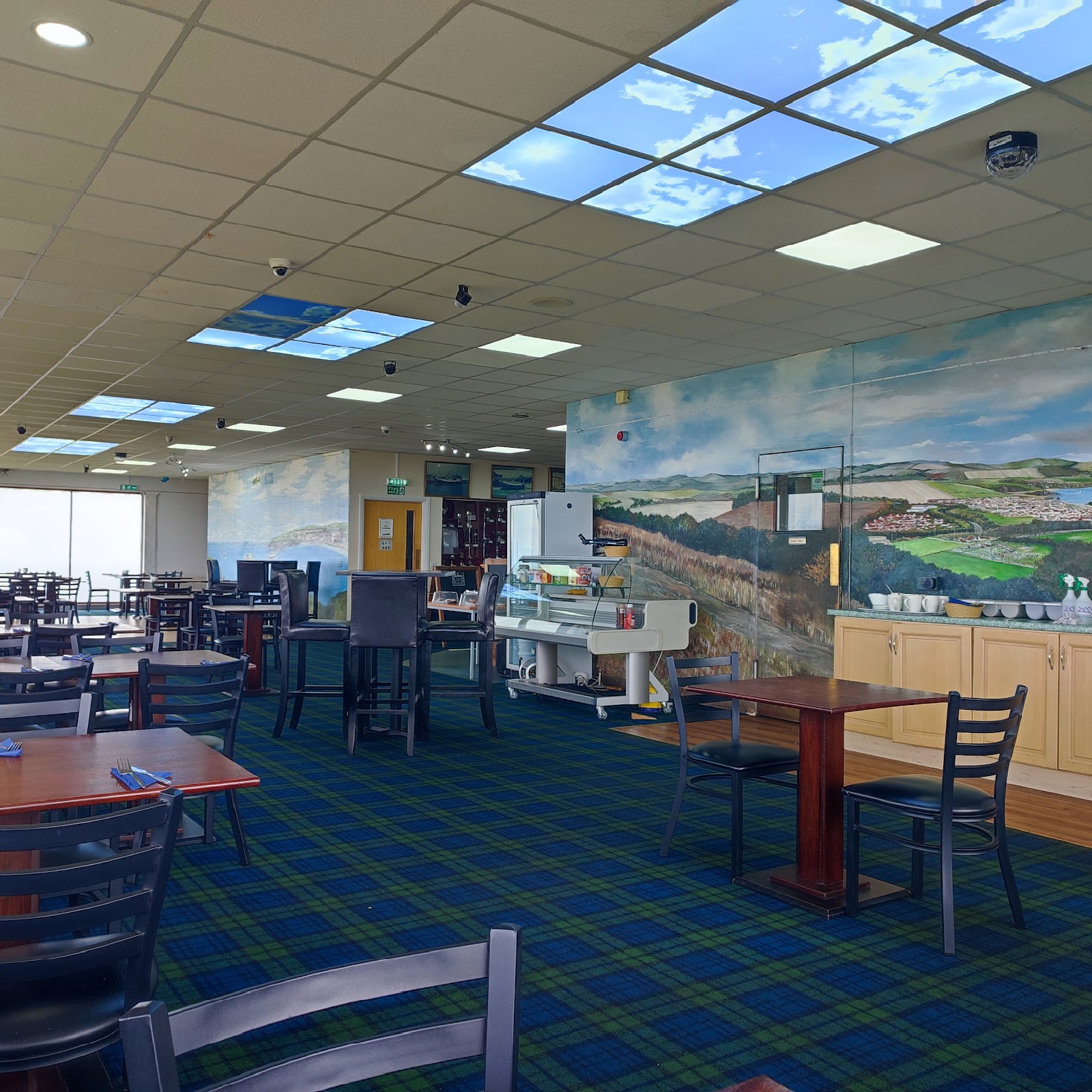 The bright dining room of the Clubhouse at Eyemouth, tables and chairs below a coastal mural and windows to the sea.