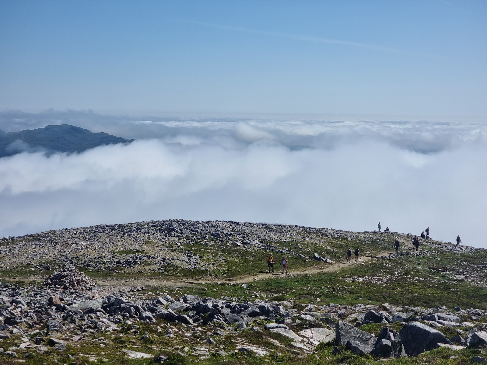 Walkers on the bouldery summit ridge of Schiehallion above a sea of cloud.