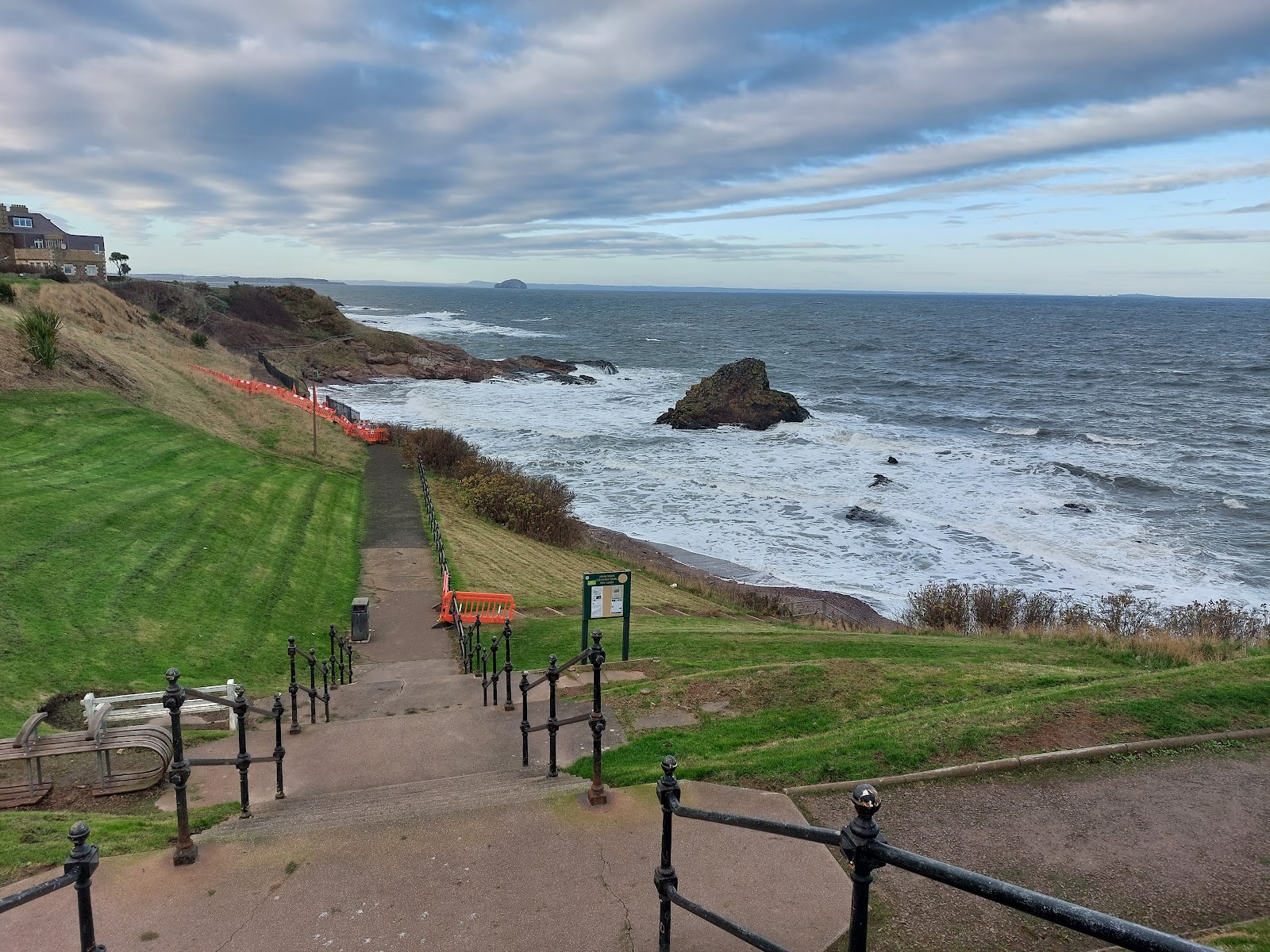 Railed path leads from grassy clifftop down to a rocky shoreline