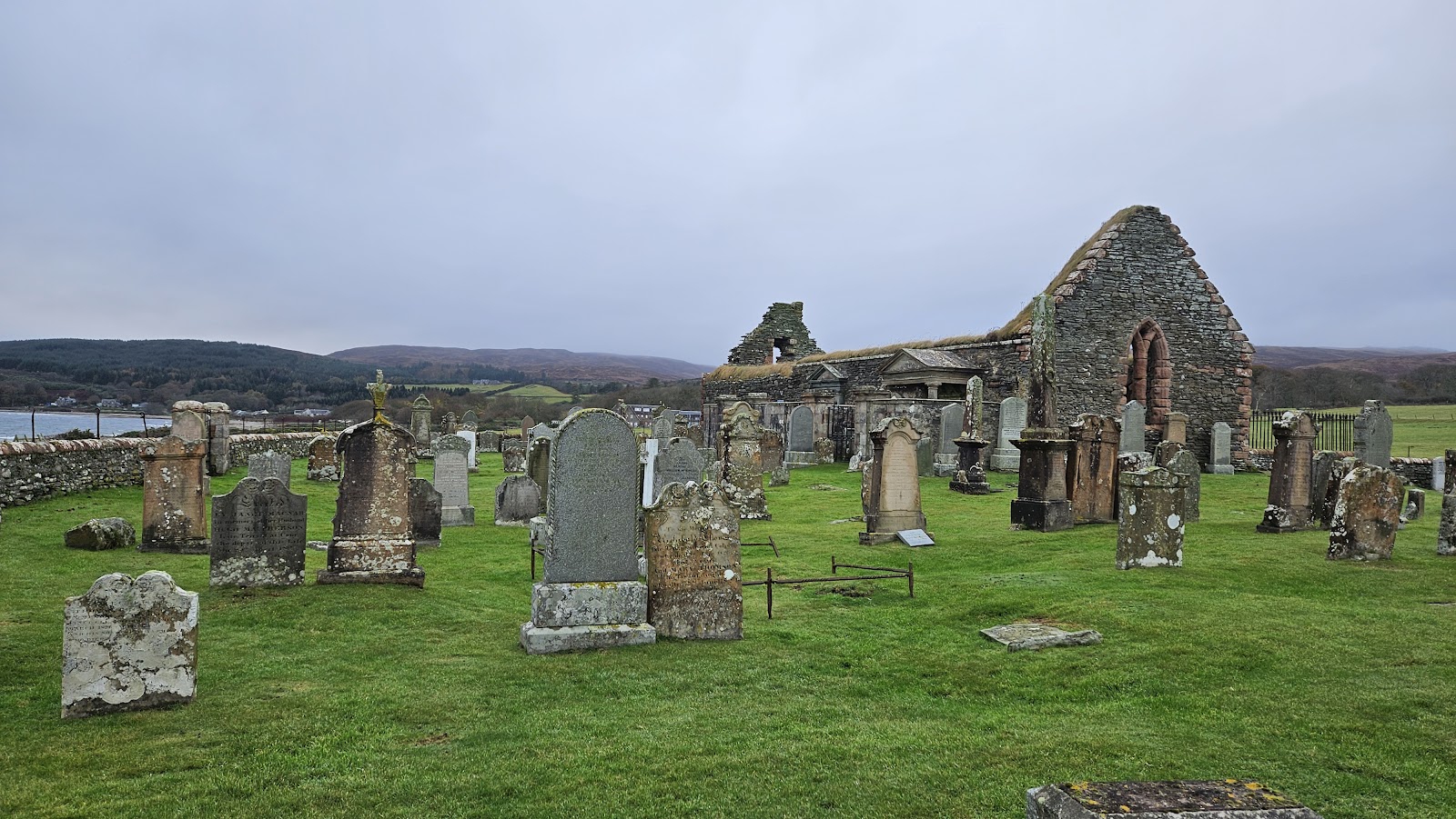 Weathered gravestones surround a roofless ruined church beside a coastal bay