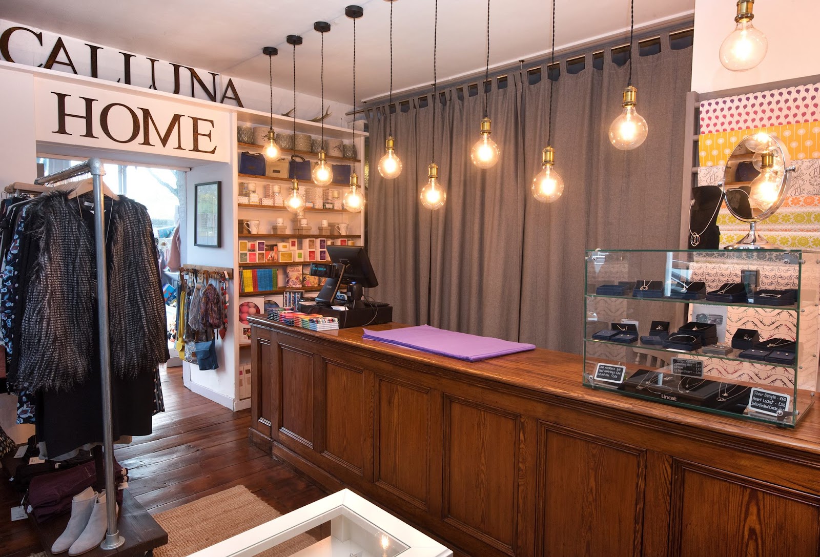 Inside Calluna in Cromarty, rails of clothes and a wooden counter under hanging bulbs.