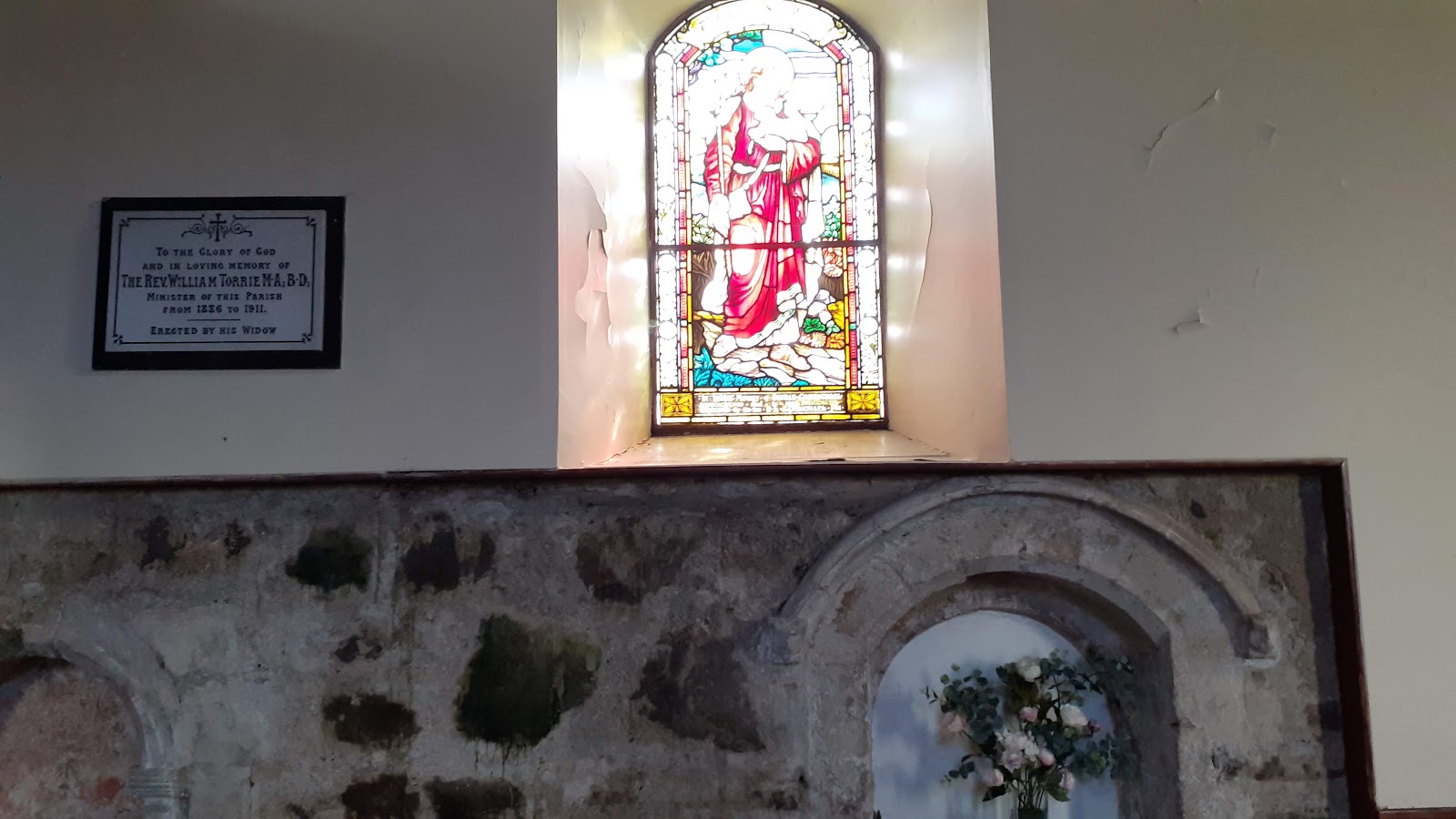 A stained-glass window above old stonework inside the church.
