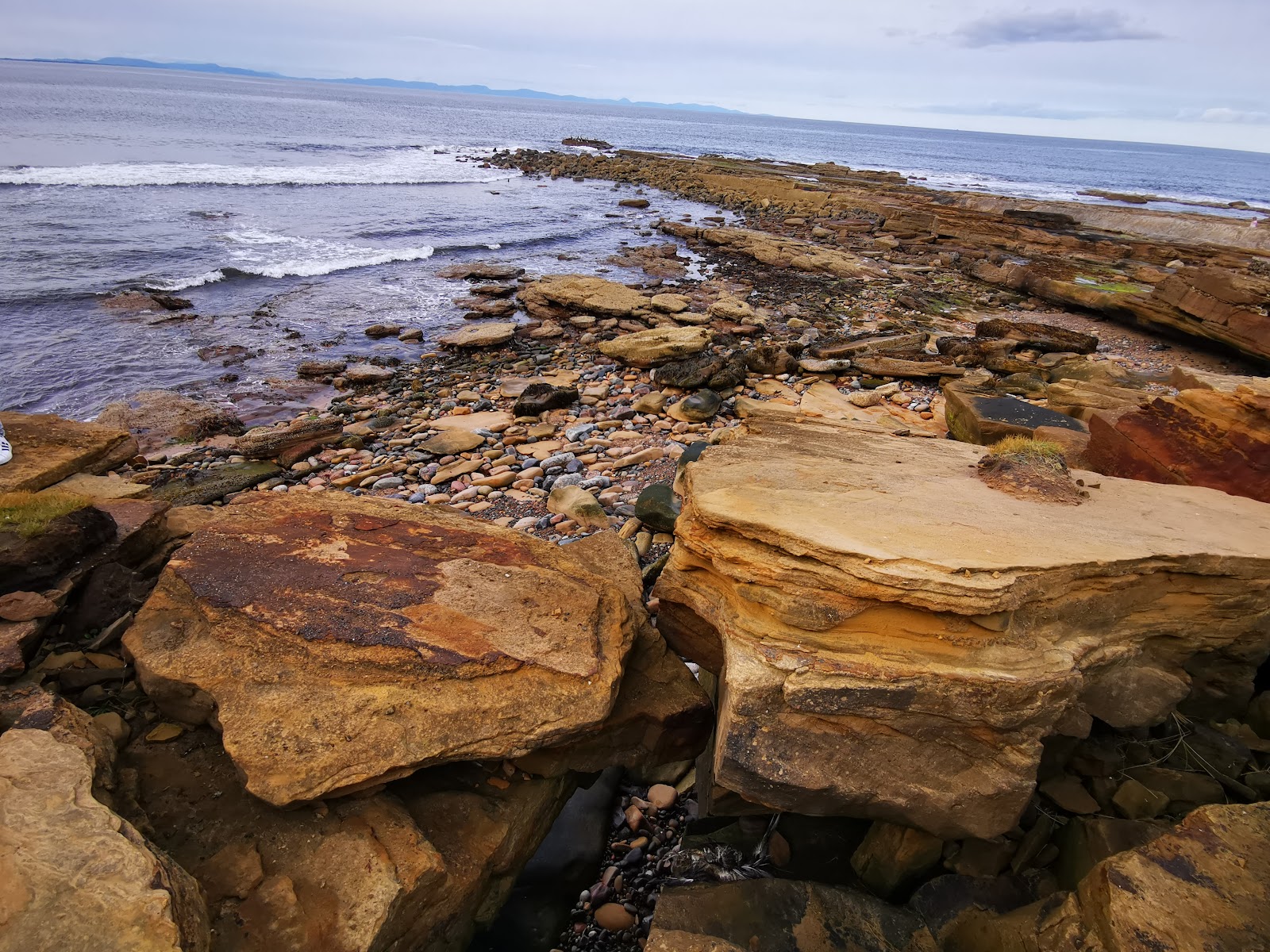 Sandstone rock formations and pebbles along a shoreline with waves breaking